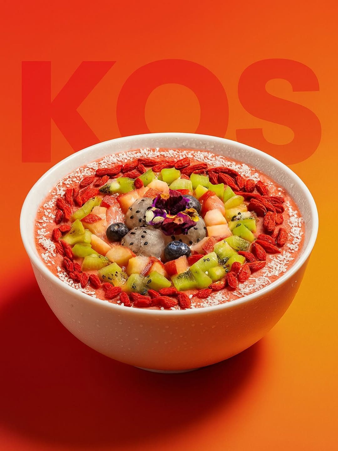 Smoothie bowl topped with kiwi, dragon fruit, goji berries and coconut on a bright orange background